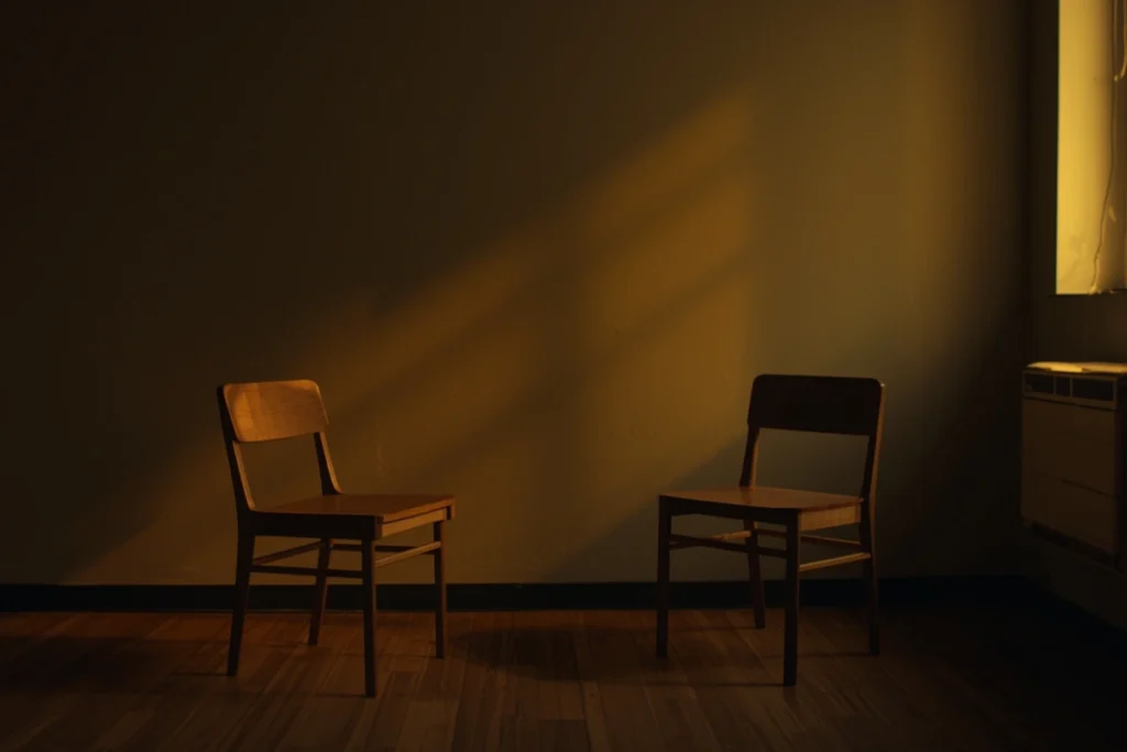 Two chairs facing each other in softly lit room, one empty, warm window light illuminating the empty chair