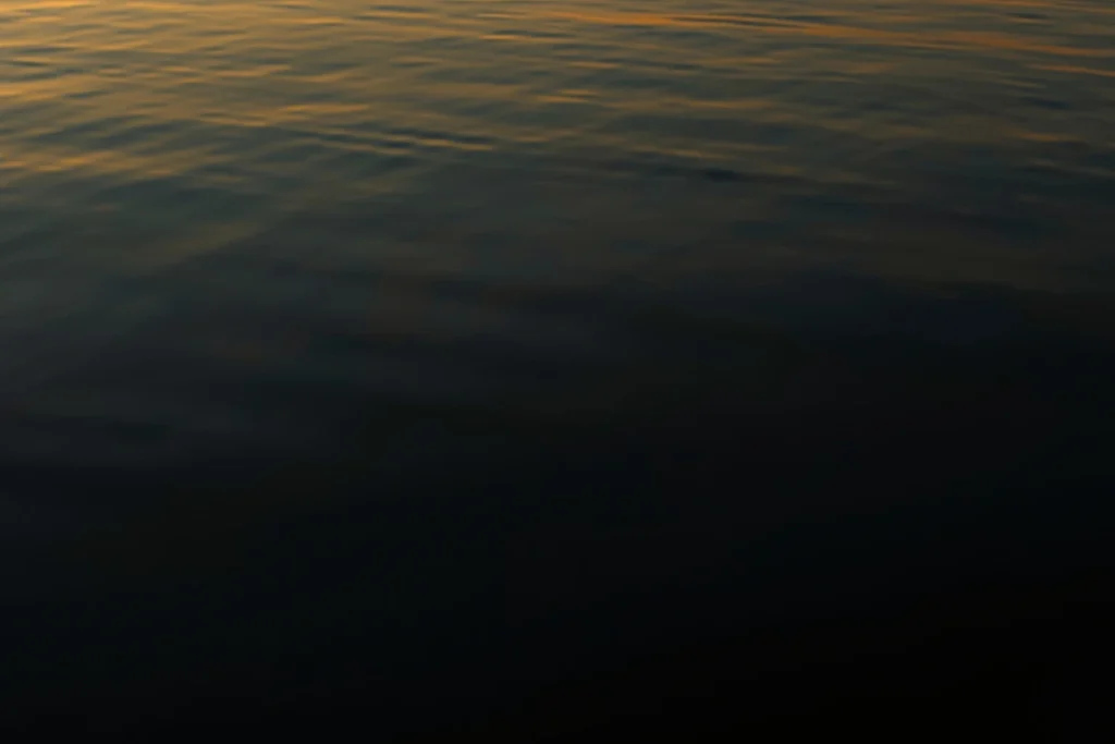 Still dark water at dusk with smooth reflective surface, soft warm light at edge, atmospheric scene