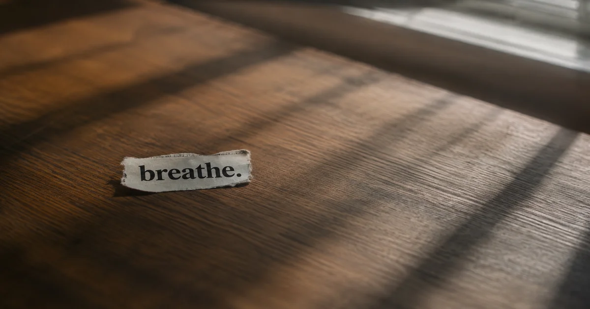 A single word torn from a newspaper page resting on a wooden table beside a blank page in soft window light