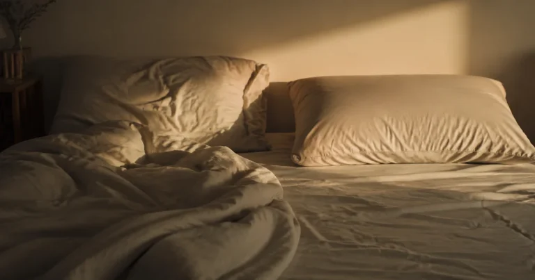 Two pillows on a bed, one undisturbed, in soft evening light