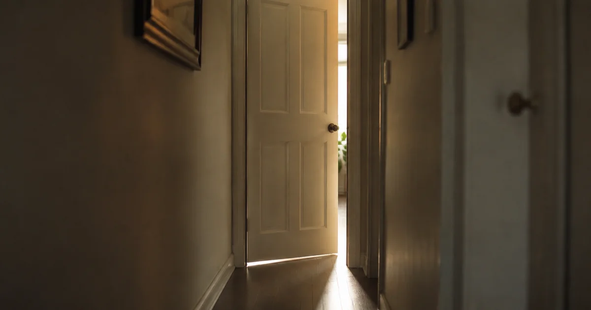 A narrow hallway doorway left slightly ajar in soft afternoon light
