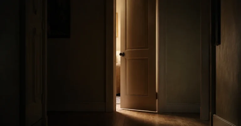 A dim hallway with one door slightly ajar and soft light spilling through the gap