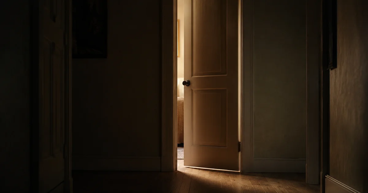 A dim hallway with one door slightly ajar and soft light spilling through the gap