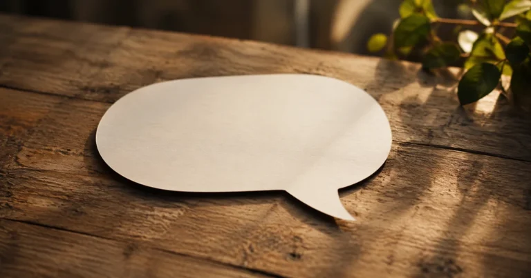 An empty speech-bubble-shaped paper cutout resting on a wooden table in soft natural light