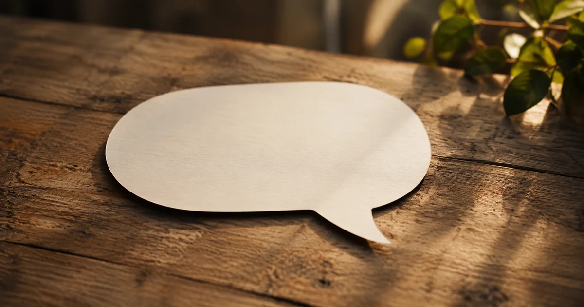 An empty speech-bubble-shaped paper cutout resting on a wooden table in soft natural light