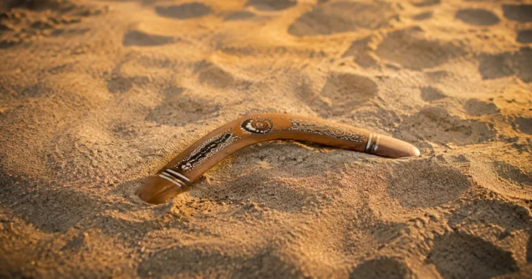 A single boomerang resting on sand after returning to where it was thrown in soft late-afternoon light