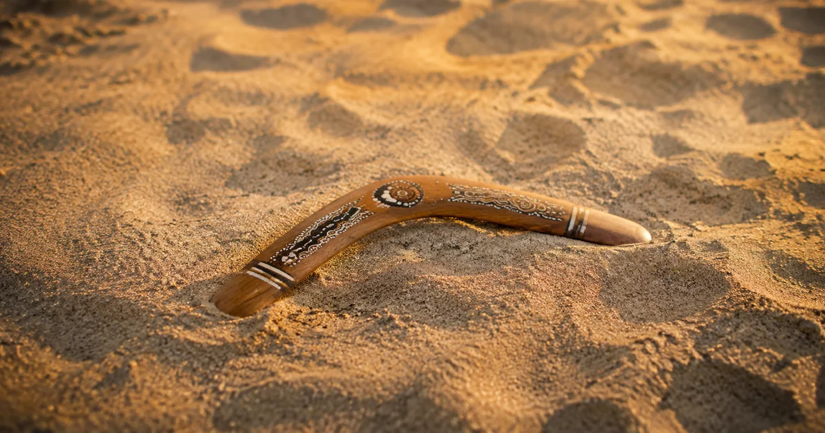 A single boomerang resting on sand after returning to where it was thrown in soft late-afternoon light