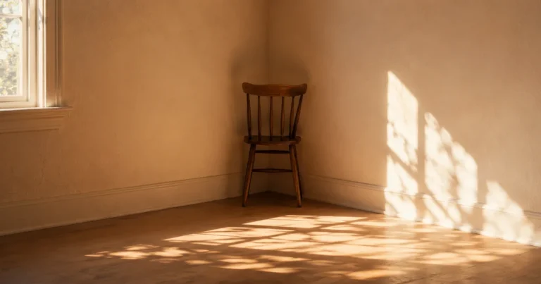 A single wooden chair facing into the corner of an empty, sunlit room