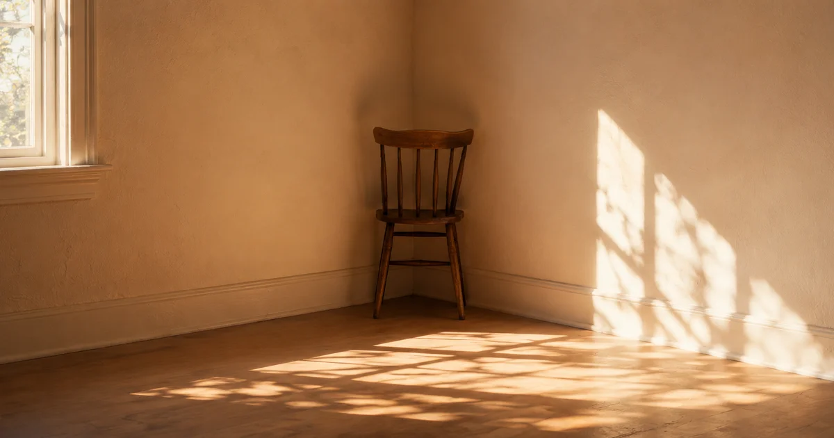 A single wooden chair facing into the corner of an empty, sunlit room