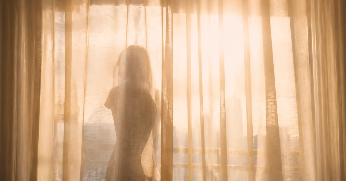 Blurred silhouette barely visible through a sunlit curtain, shape almost invisible against bright glass