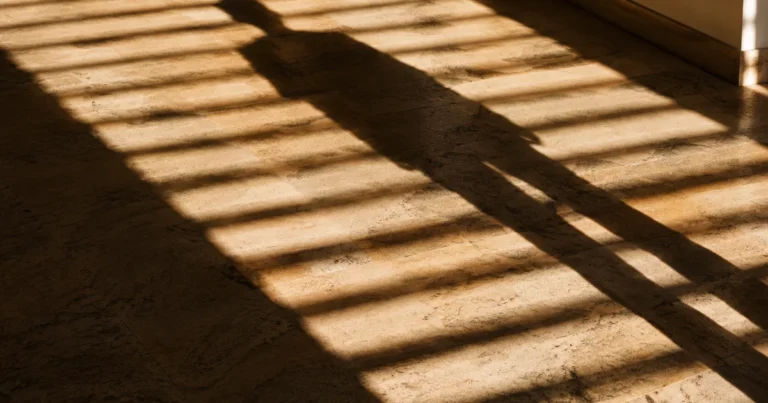 Long shadow cast across a sunlit floor by venetian blinds, striped light pattern