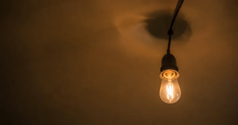 Light bulb on a string flickering mid-glow against a plain ceiling