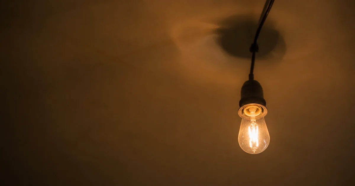 Light bulb on a string flickering mid-glow against a plain ceiling