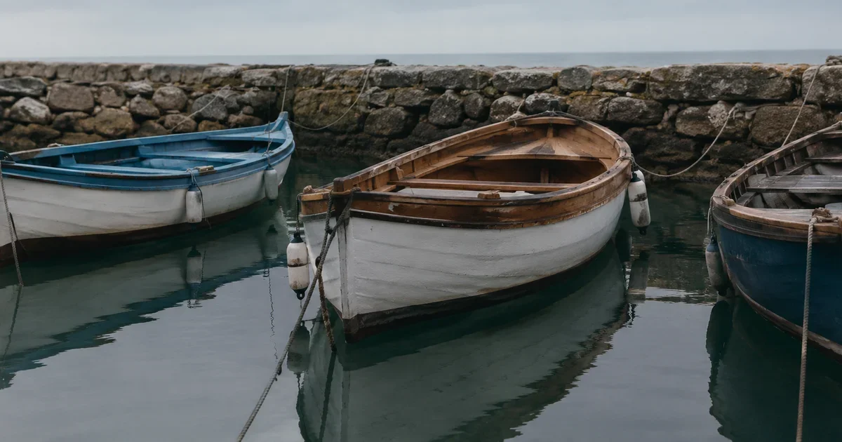 Three small wooden boats resting closely and calmly at anchor in a sheltered harbor, a stone breakwater behind them