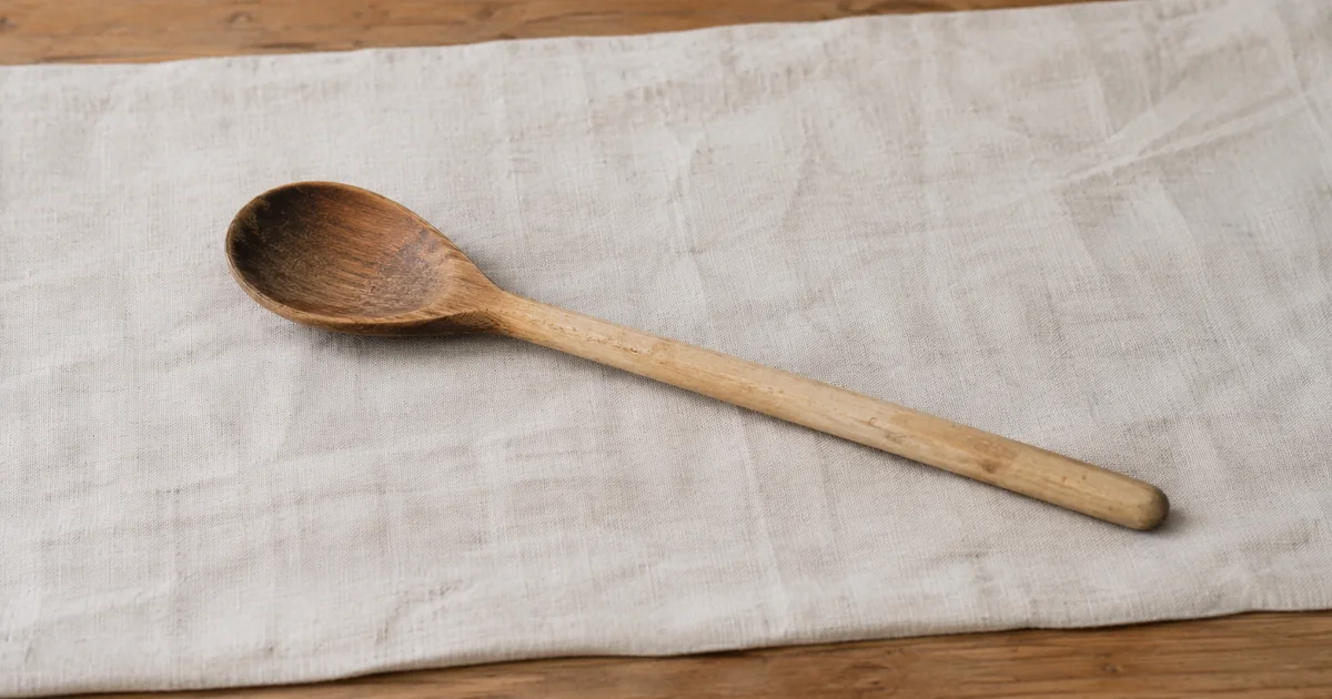 A single old wooden spoon, its handle worn smooth, resting alone on a plain linen cloth.
