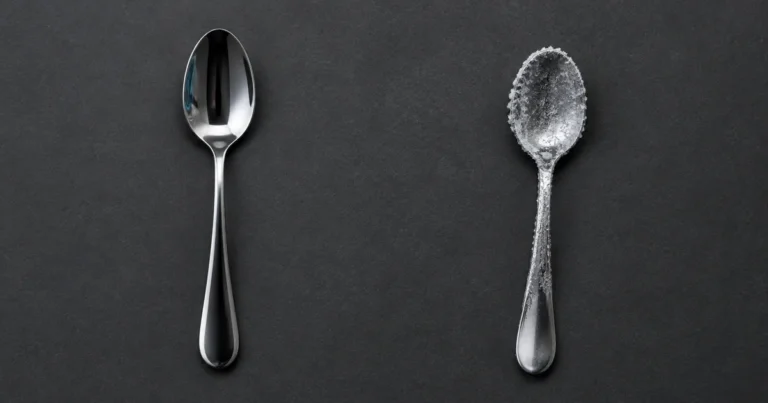 Two plain steel teaspoons on a dark gray surface, the left one clean and polished, the right one partly covered in frost