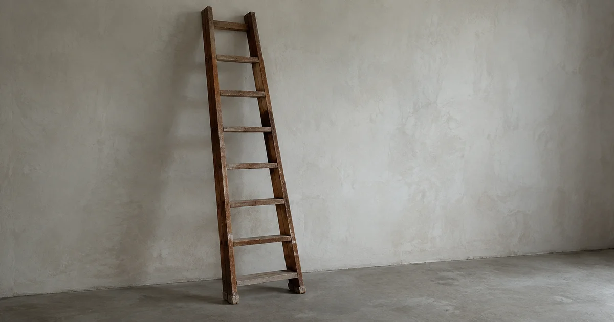 A wooden ladder leaning against a plain wall in a bare, unfurnished room