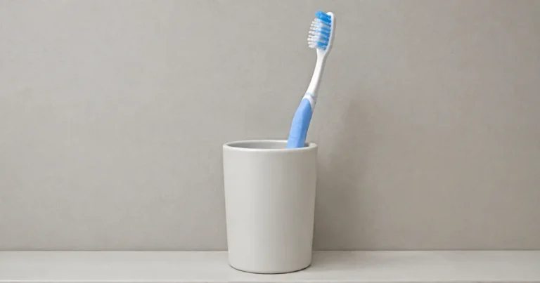 An ordinary toothbrush standing in a plain cup on a simple bathroom shelf