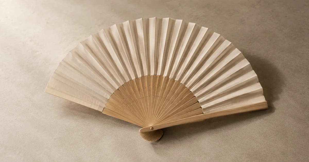 A plain folding hand fan fully open on a neutral surface, with its ribs and pleats clearly visible